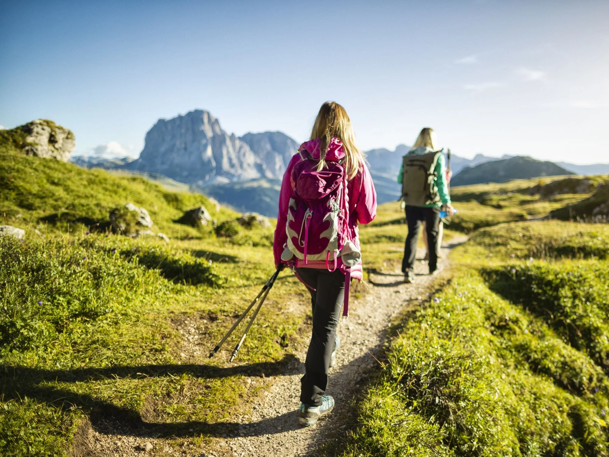 Two hikers with backpacks on a meadow trail facing the Sassolungo peak in the Italian Dolomites