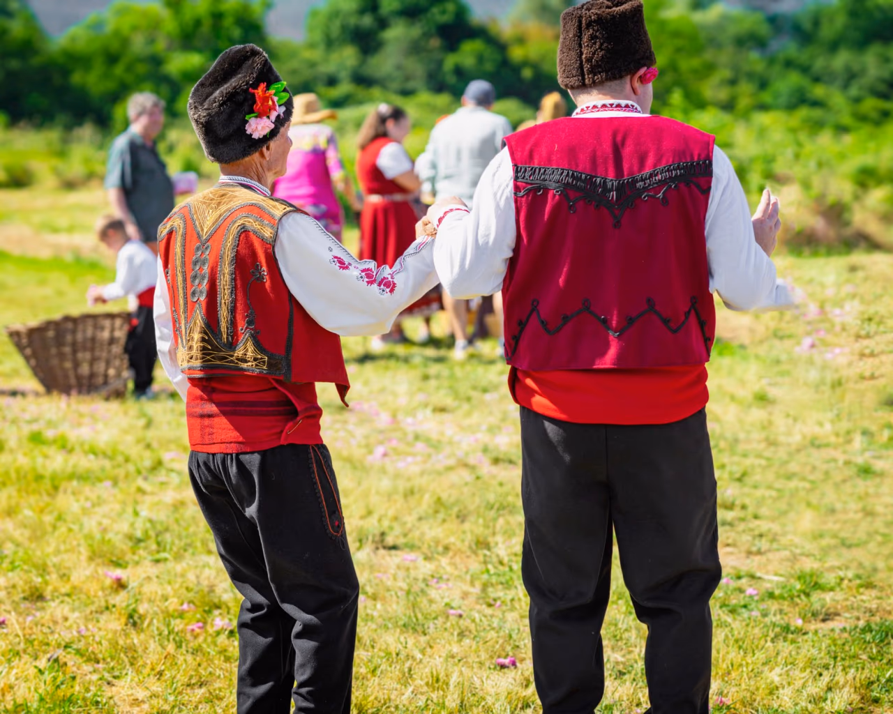 Bulgarian men in traditional folk costumes dancing at a cultural festival outdoors.