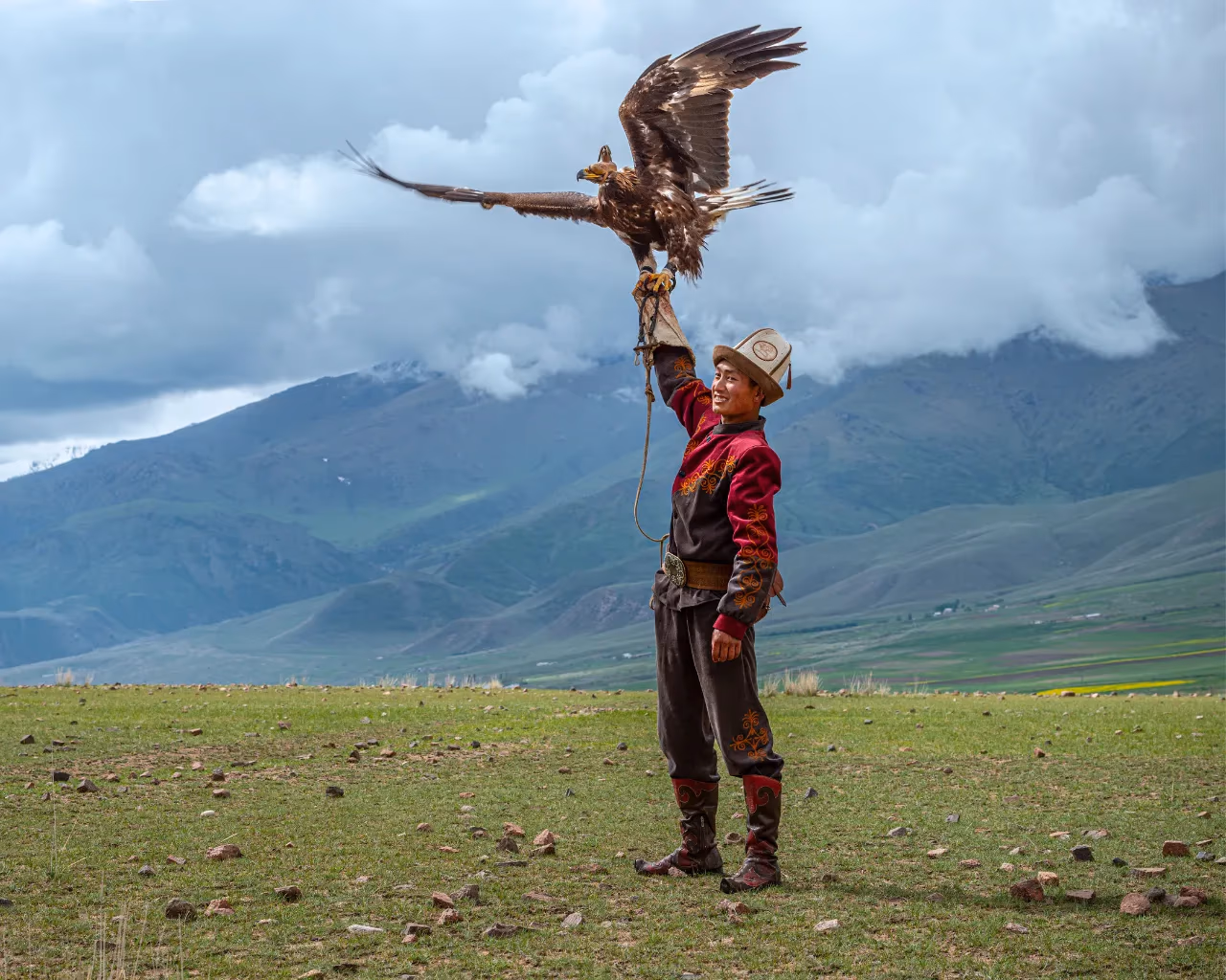 Kyrgyzstan Eagle Hunter - Kyrgyz hunter in traditional attire raising a golden eagle in an open field.