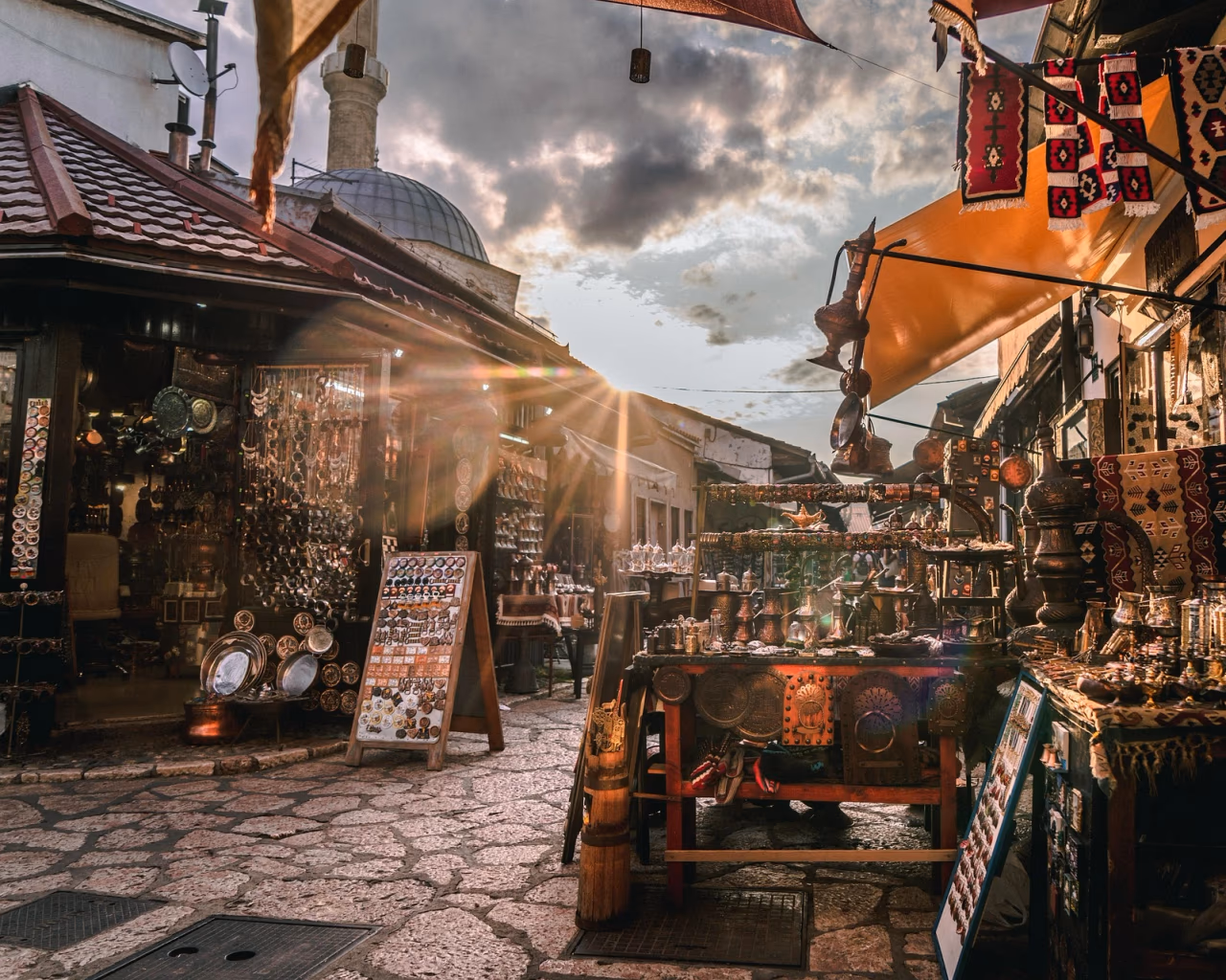 Sunlit Baščaršija bazaar in Sarajevo lined with stalls selling copperware, carpets and souvenirs.