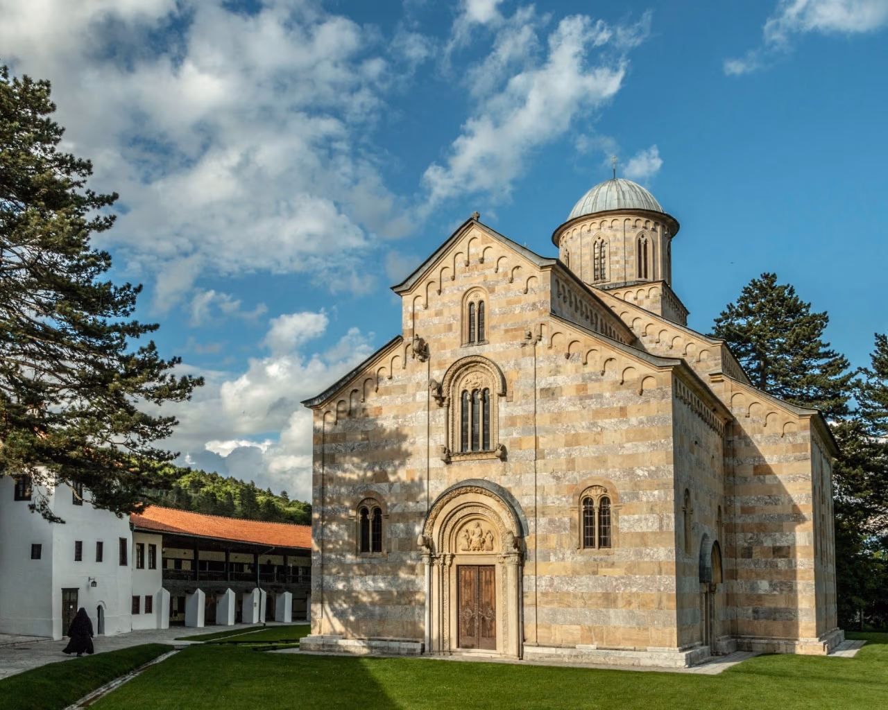 Striped stone Visoki Dečani Monastery with domed roof surrounded by pine trees in Kosovo.