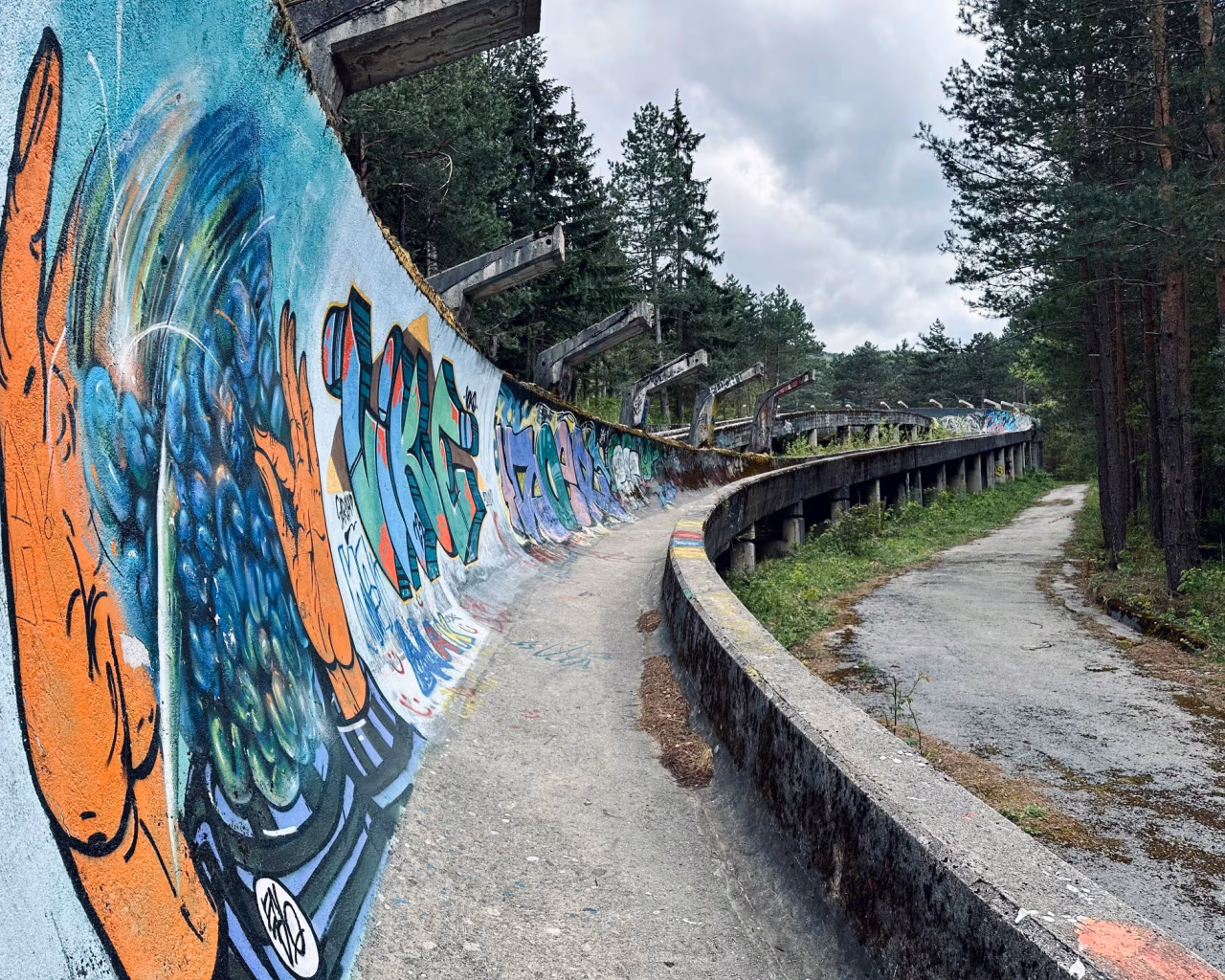 Abandoned graffiti-covered bobsleigh track winding through pine forest on Mount Trebević near Sarajevo.