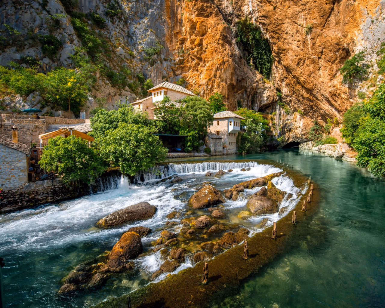 Blagaj Tekke monastery beside turquoise Buna River, cliffs and cascading waterfalls in Bosnia and Herzegovina.