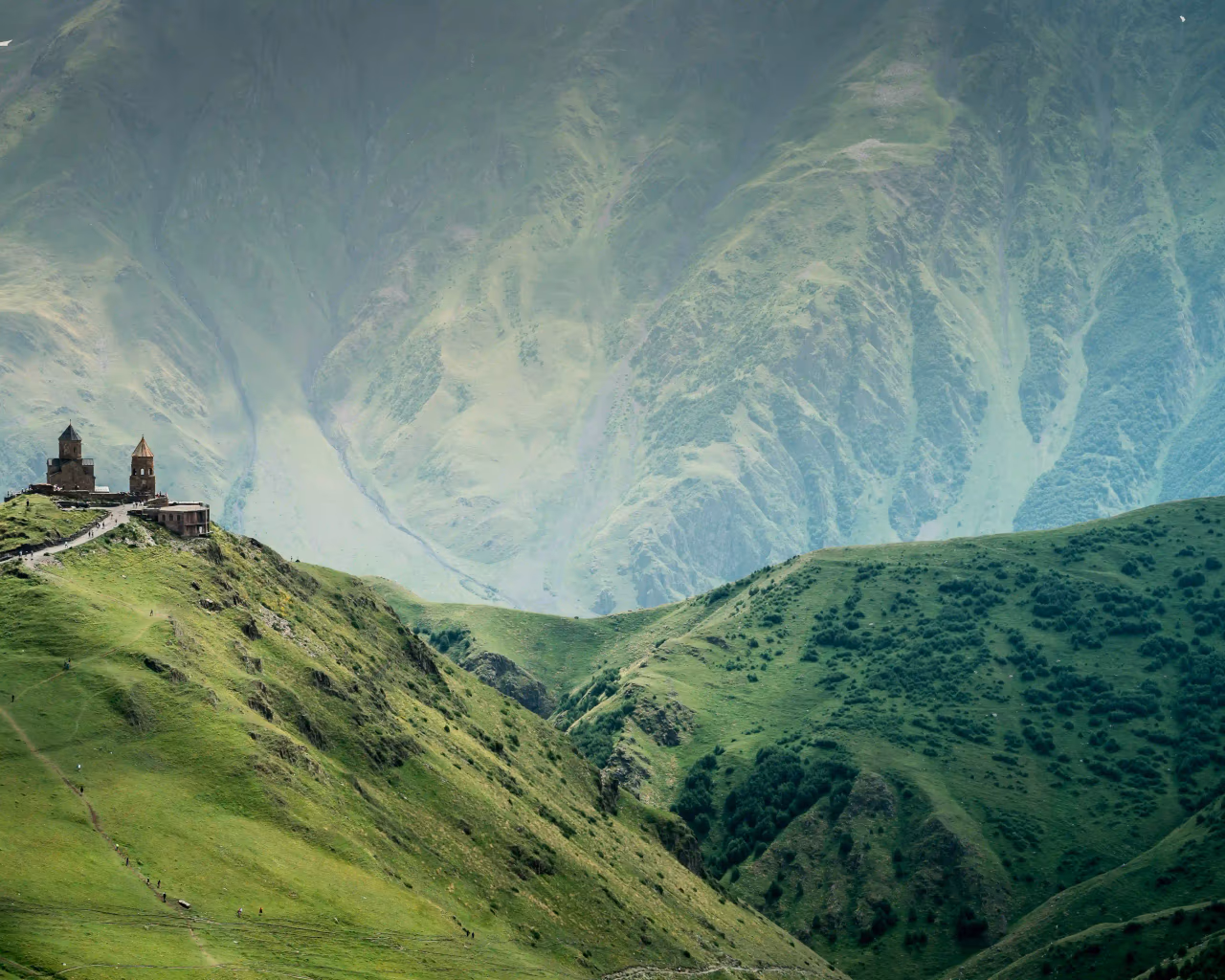Gergeti Trinity Church atop a green hill in Georgia, surrounded by towering misty mountains.