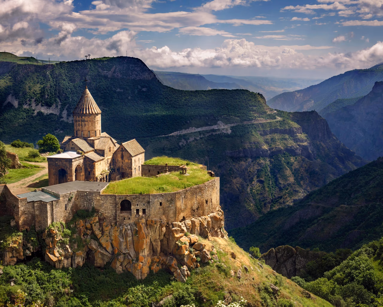 Tatev Monastery on a cliffside in Armenia, surrounded by lush green mountains and deep gorges.