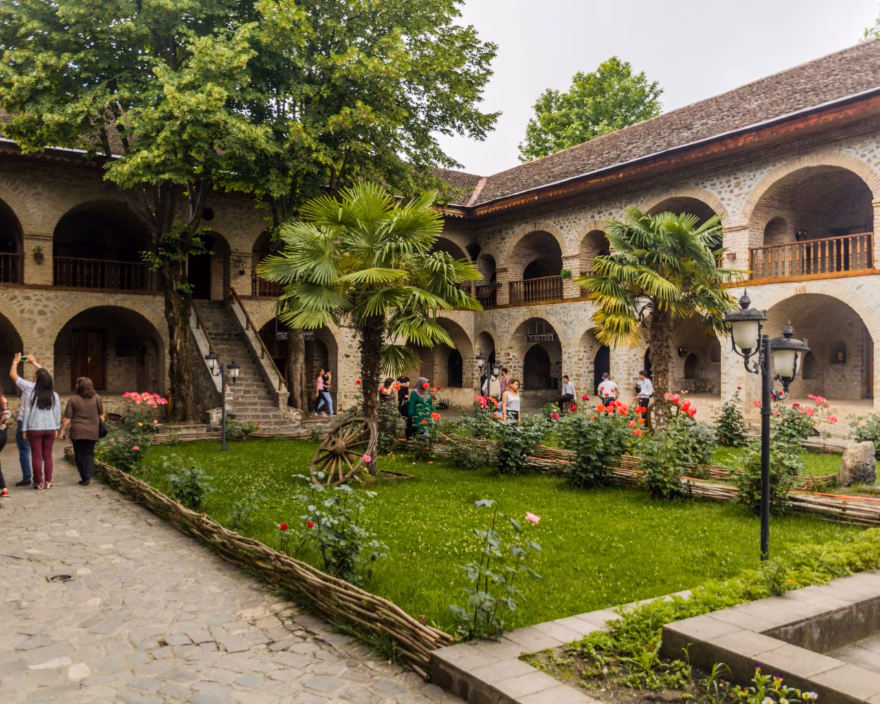 Sheki Caravanserai courtyard in Azerbaijan with stone arches, palm trees, and blooming garden