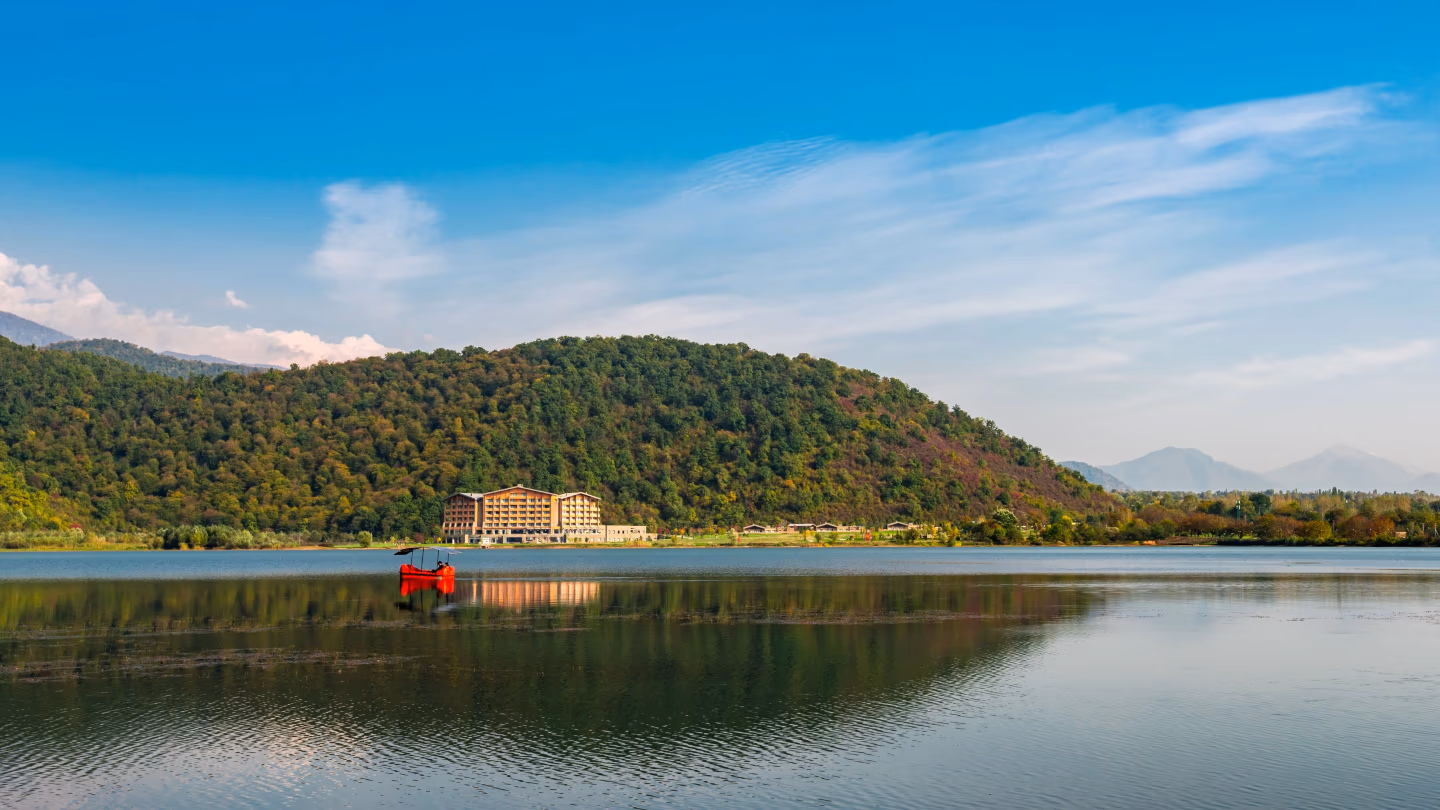 Scenic view of Lake Göygöl in Azerbaijan with forested hills, reflection on the water, and red boat
