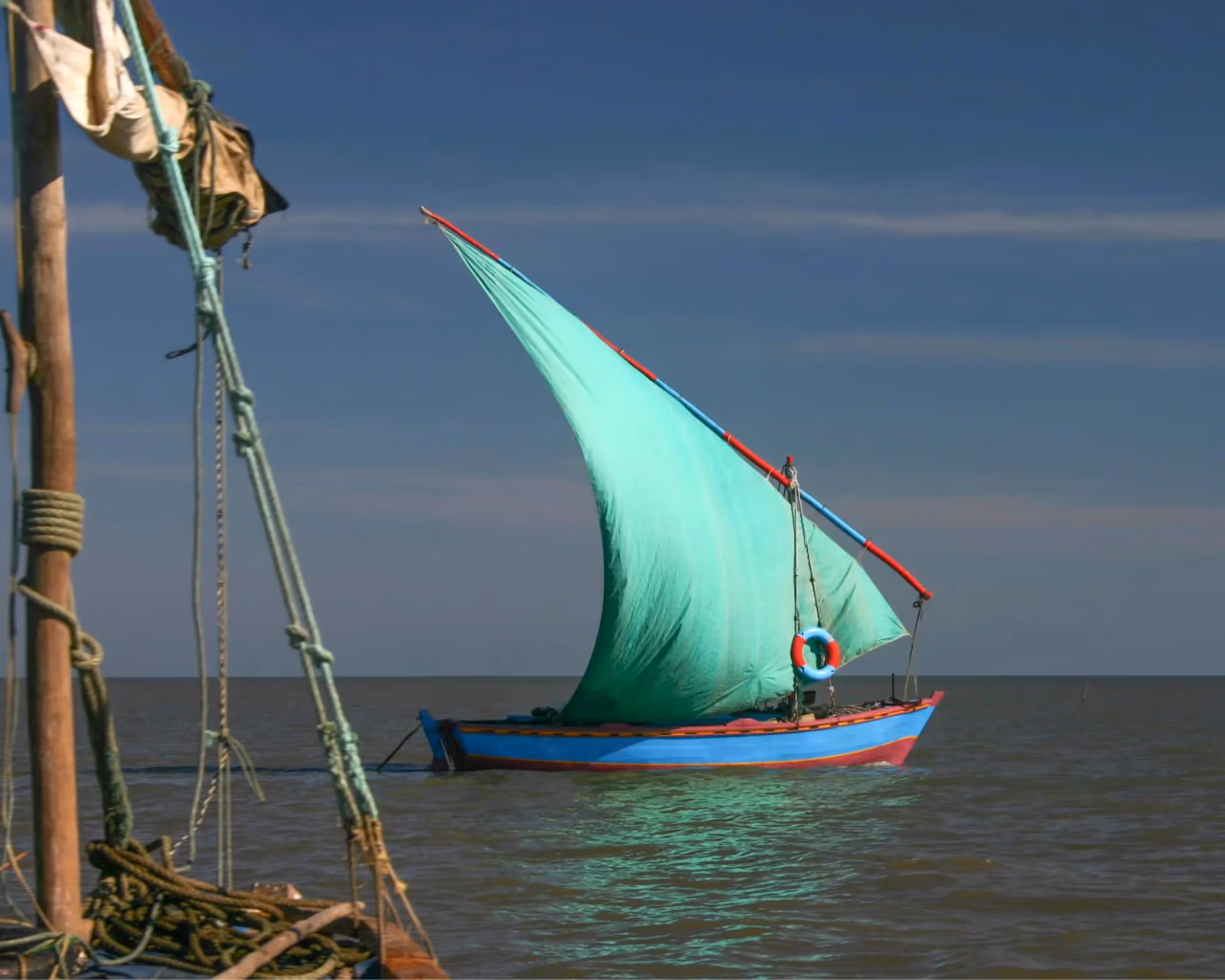Blue dhow with a billowing turquoise triangular sail crossing calm open water off the Mozambique coast