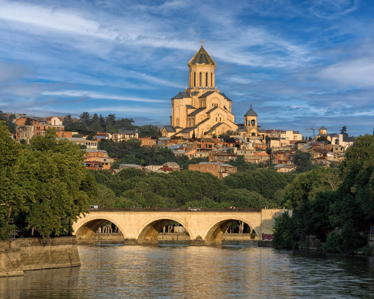 Tbilisi's Holy Trinity Cathedral (Sameba) towering above the Mtkvari River, with a stone arched bridge in front