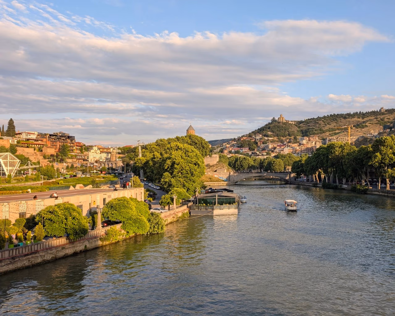 Mtkvari River winding through Tbilisi's Old Town, with hillside houses and the distant Narikala Fortress