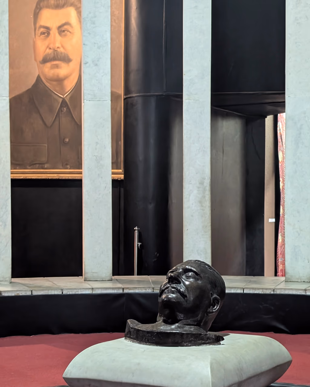 Joseph Stalin Museum – bronze bust of Joseph Stalin on a marble pedestal with a large portrait of Stalin behind in Gori, Georgia.