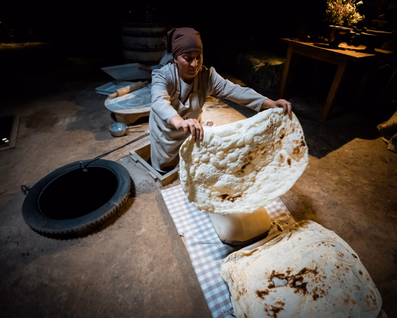 Armenian lavash making – woman baking traditional lavash bread over a tandoor oven in a rustic village bakery.