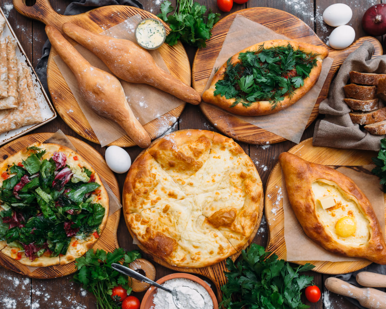 Georgian feast – overhead view of a traditional Georgian meal with khachapuri bread, salads, herbs and eggs.