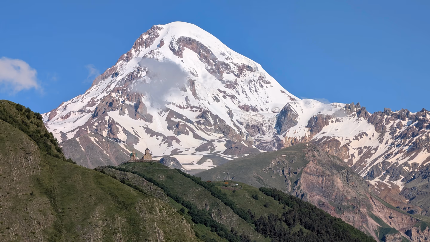 Mount Kazbek Georgia – snow‑capped Mount Kazbek towering over lush green hills and a tiny church in the Kazbegi region.