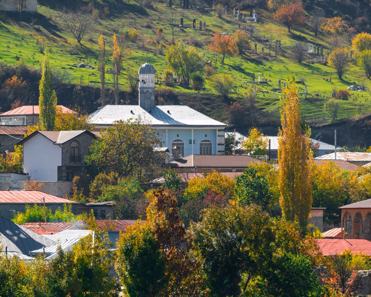 Caucasus village scene – autumn hillside village with colorful trees and a white domed church in the Caucasus mountains.