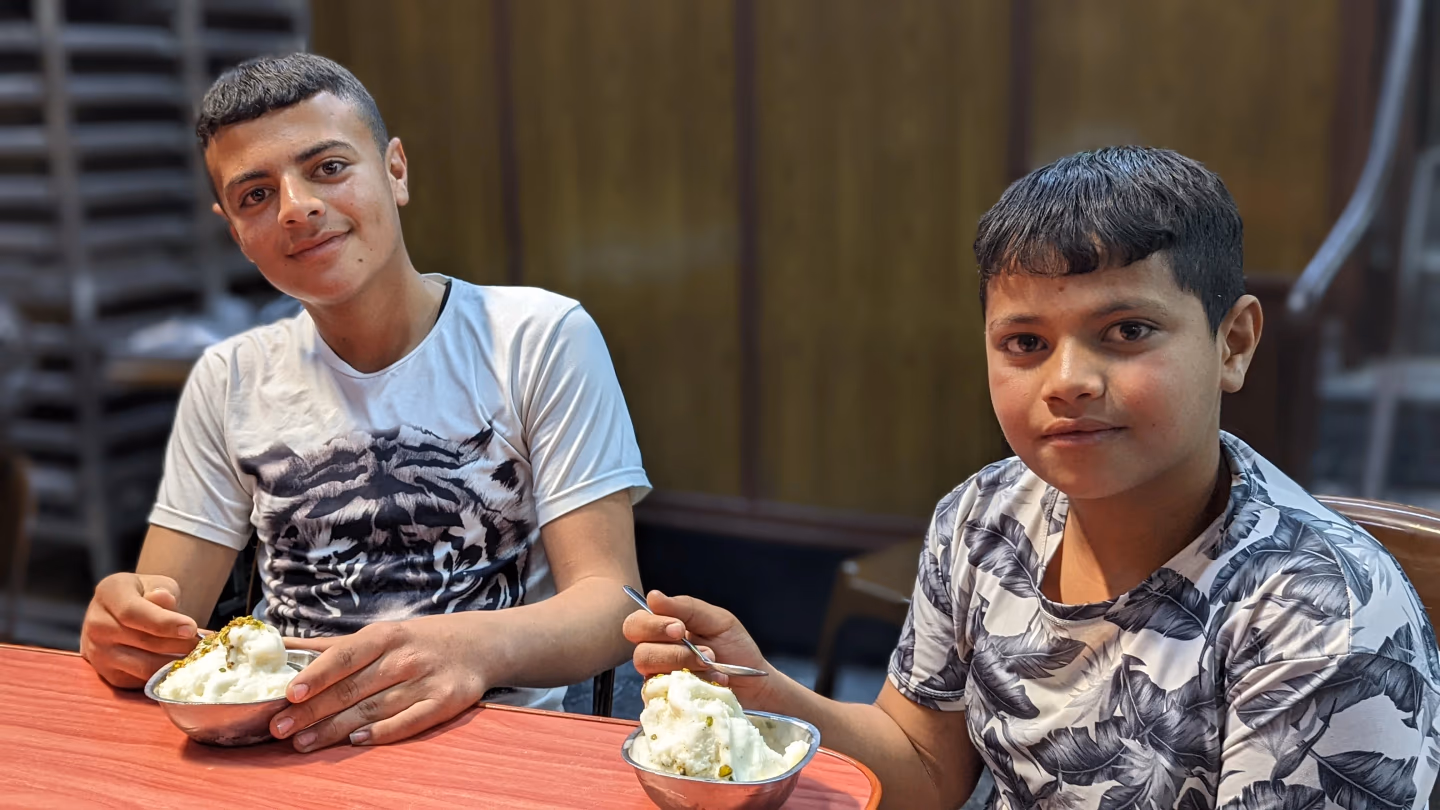 Two boys smiling while enjoying Syrian mastic ice cream topped with crushed pistachios