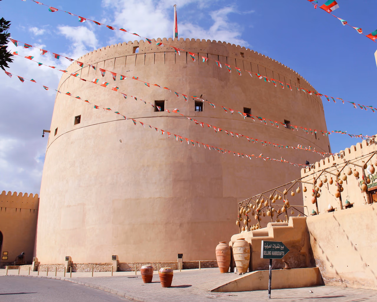 The grand round tower and clay-brick architecture of Nizwa Fort under a clear sky in Oman.