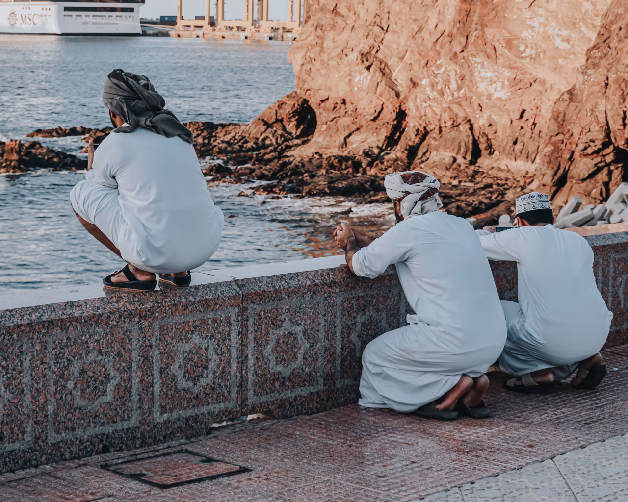 Three men in traditional Omani attire enjoying the coast on an Oman tour.
