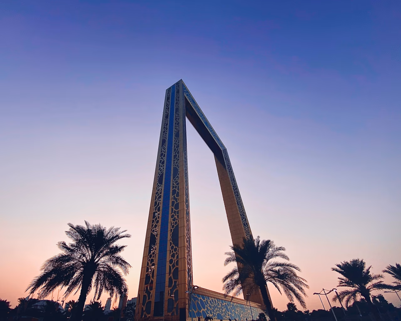 The Dubai Frame landmark at dusk with palm trees in foreground