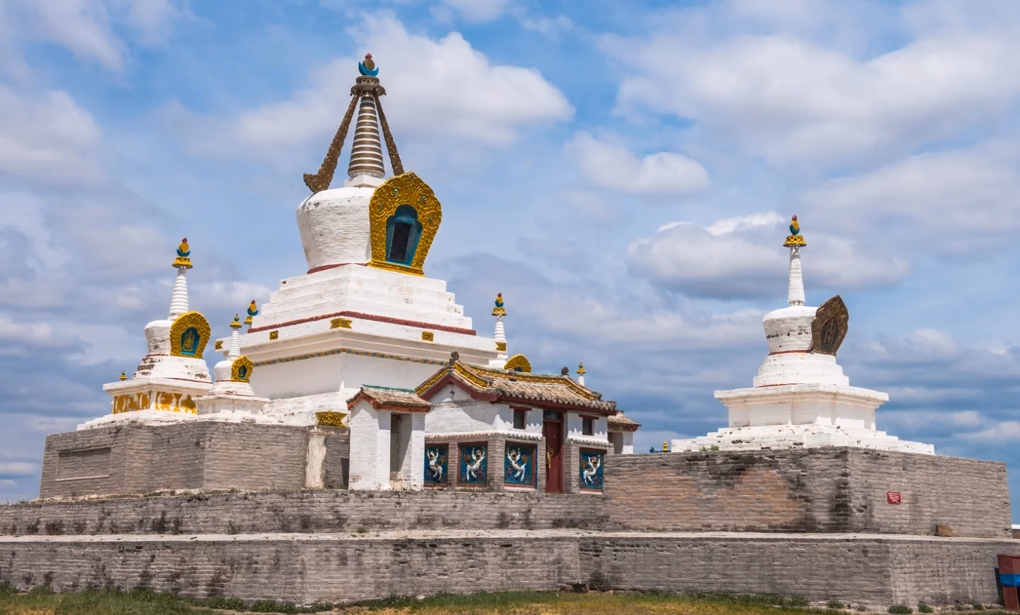 Erdenezuu Temple Mongolia, white stupas with gold trim under partly cloudy blue sky.