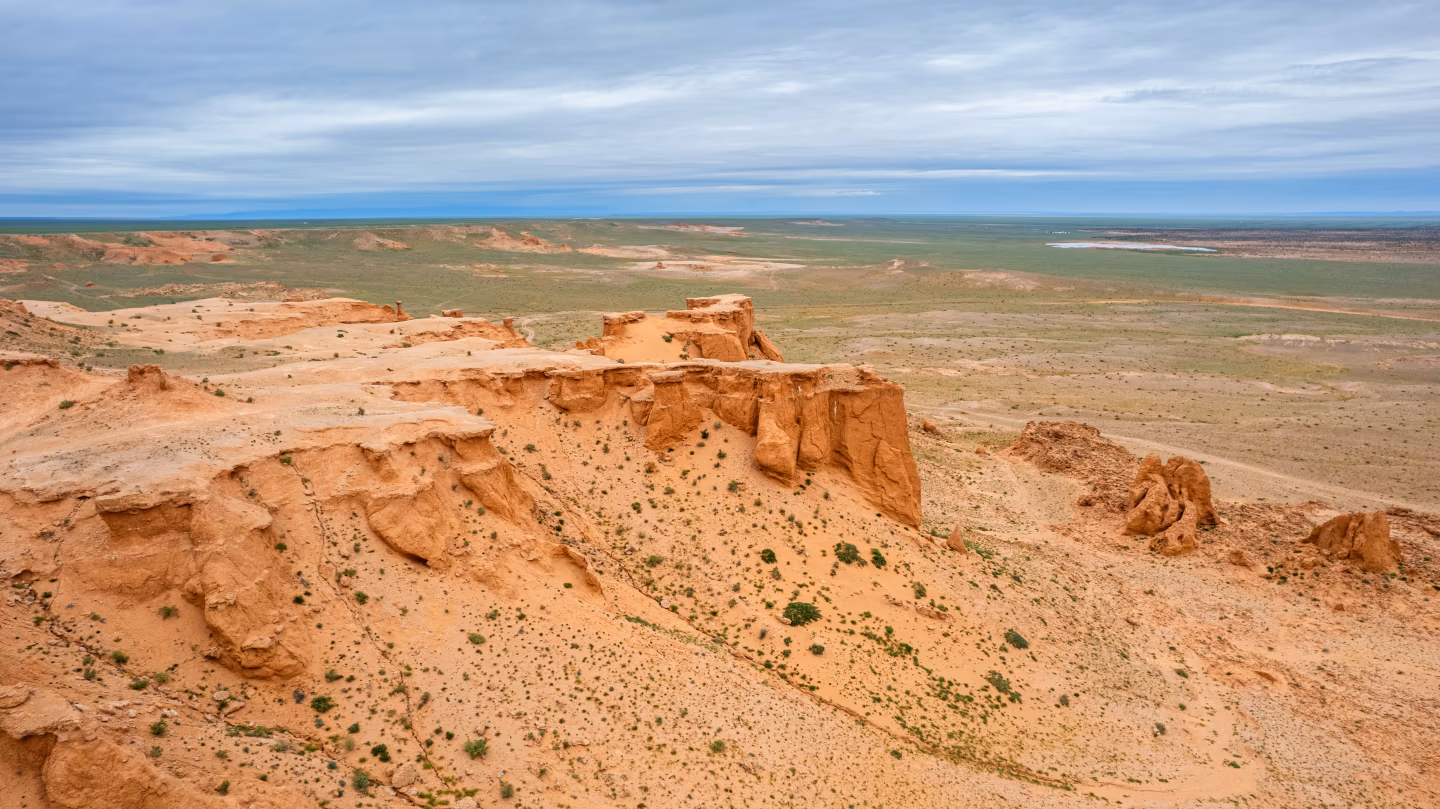 Red cliffs of Mongolia's Flaming Cliffs stretch across Gobi Desert plain.