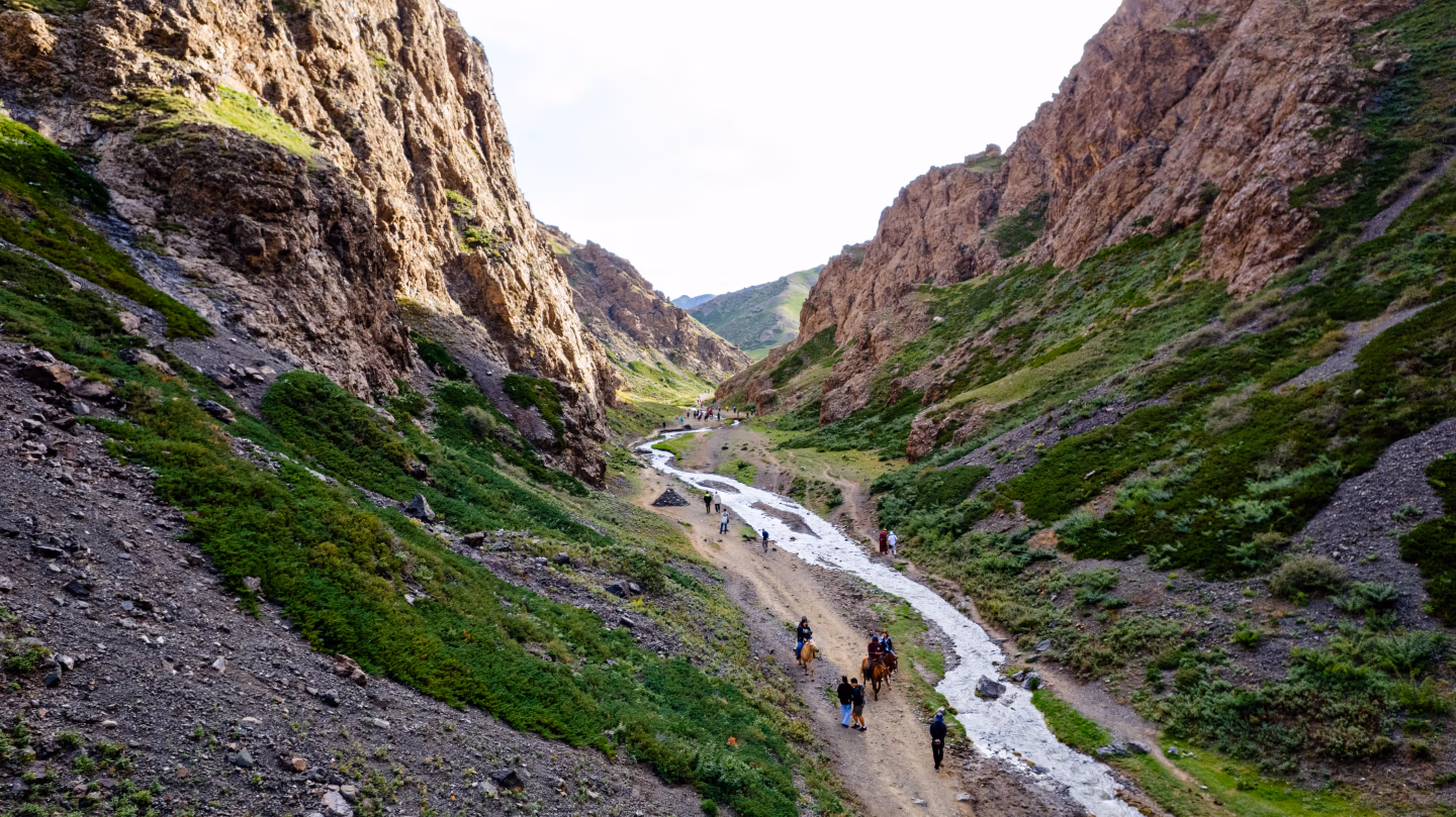 Tourists riding horses through Mongolia's Yol Valley between rocky cliffs.