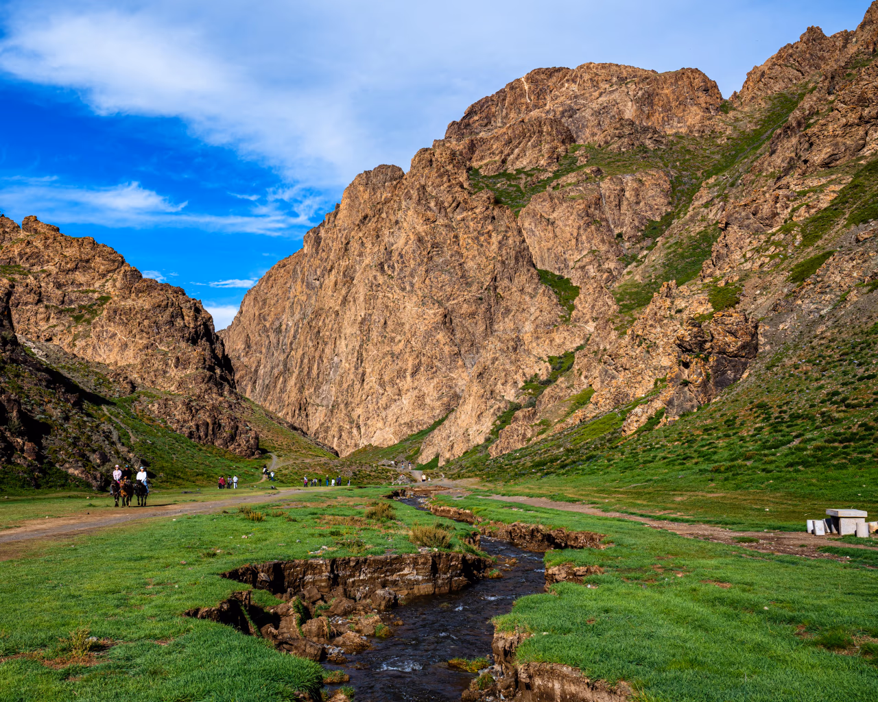 Yolyn Am gorge Mongolia with green valley, stream, brown cliffs and tourists on horseback.
