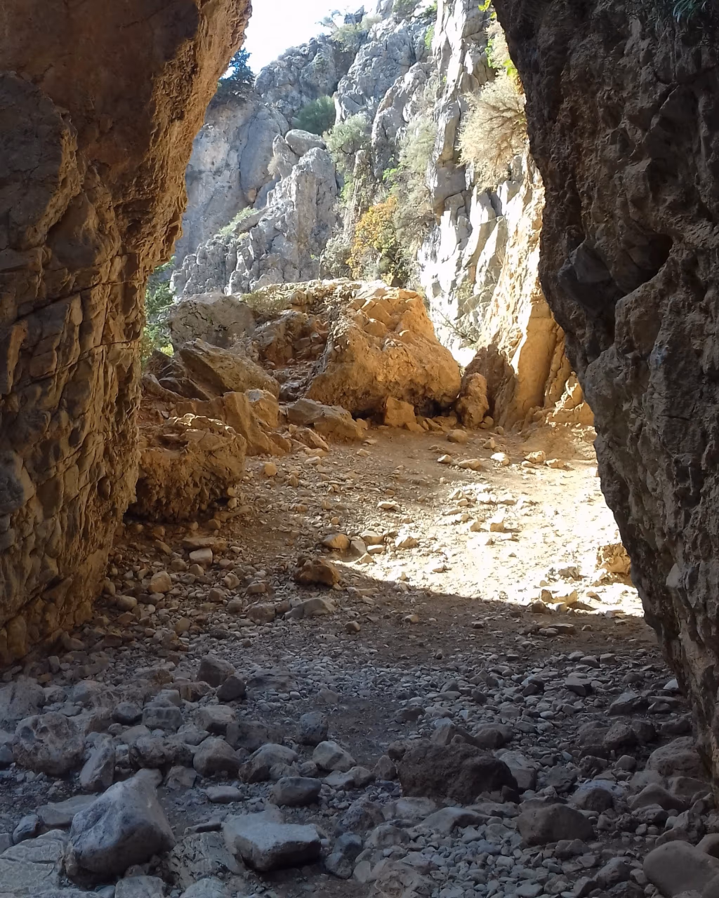 Rocky path through a natural stone arch in a sunlit mountain gorge, Crete.