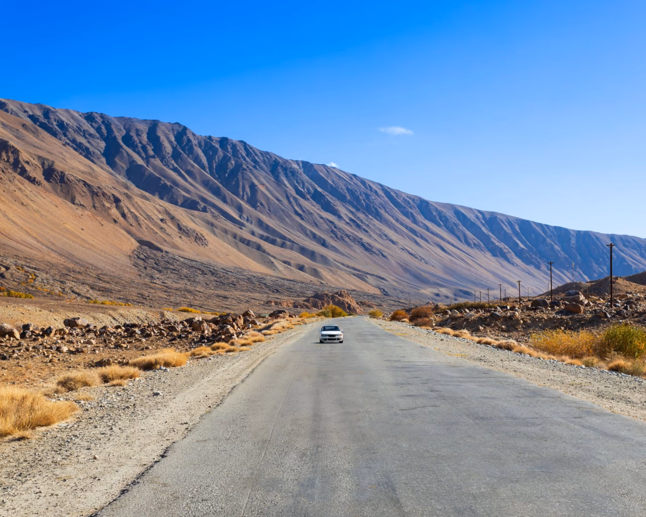 Car driving on a remote stretch of the Pamir Highway with rugged brown mountains in Tajikistan