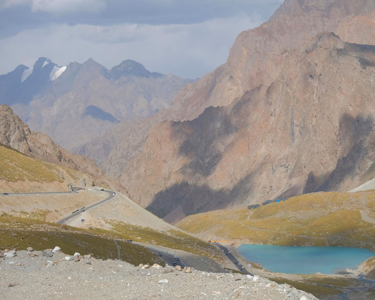 Curving road through rocky mountains with a turquoise alpine lake nestled below steep cliffs.