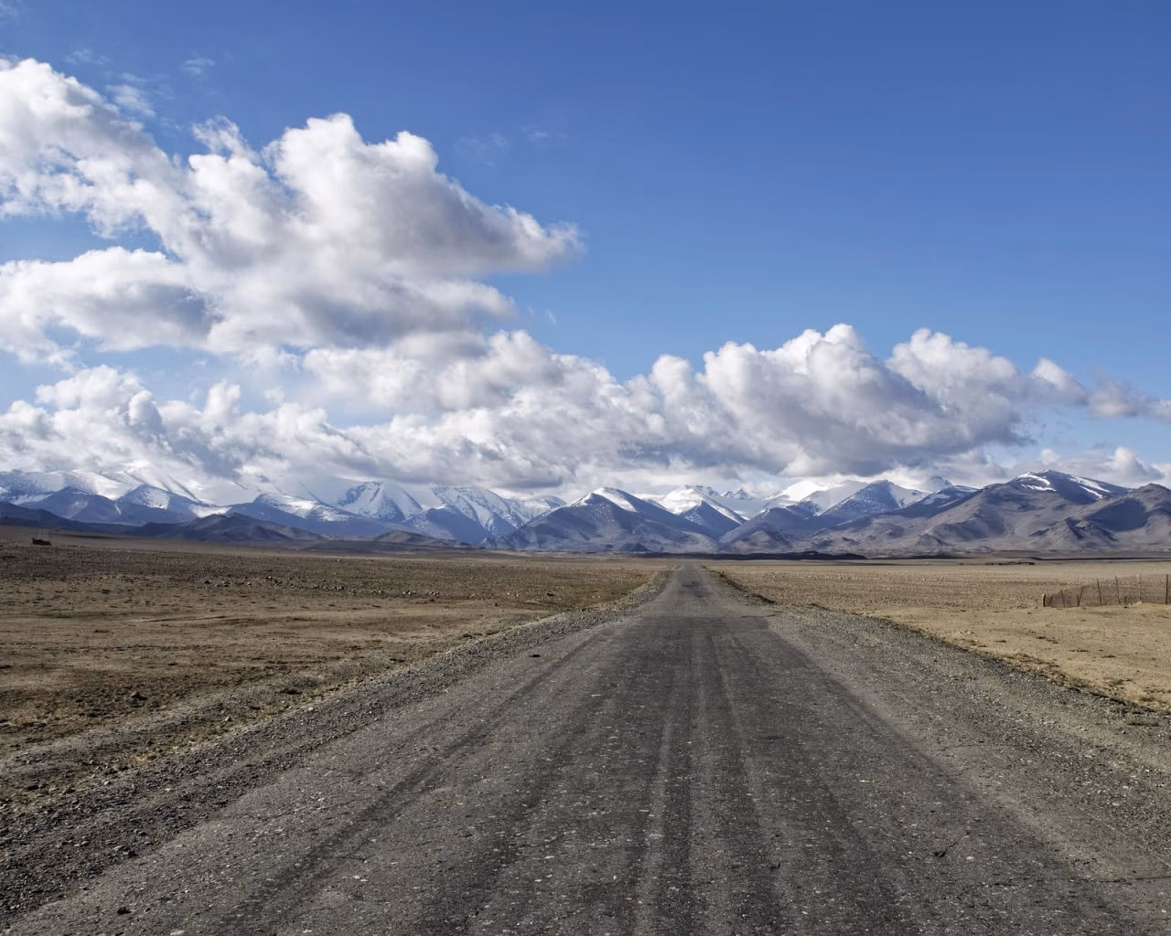 Scenic view of a vehicle navigating the winding gravel road of the Pamir Highway, surrounded by dramatic snow-capped peaks in Tajikistan