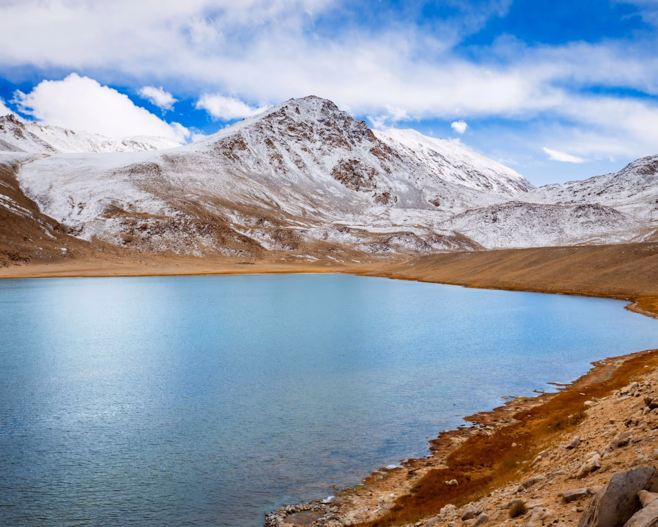 Turquoise mountain lake bordered by snow-dusted hills under a bright sky in eastern Tajikistan.