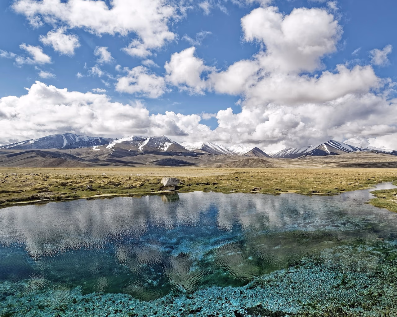 Crystal-clear alpine spring reflecting the Pamir Mountains under scattered clouds in Tajikistan.