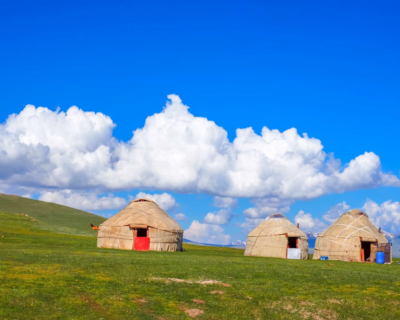 Scenic view of traditional nomadic yurts near the shores of Son-Kul Lake, surrounded by green pastures and mountains in Kyrgyzstan