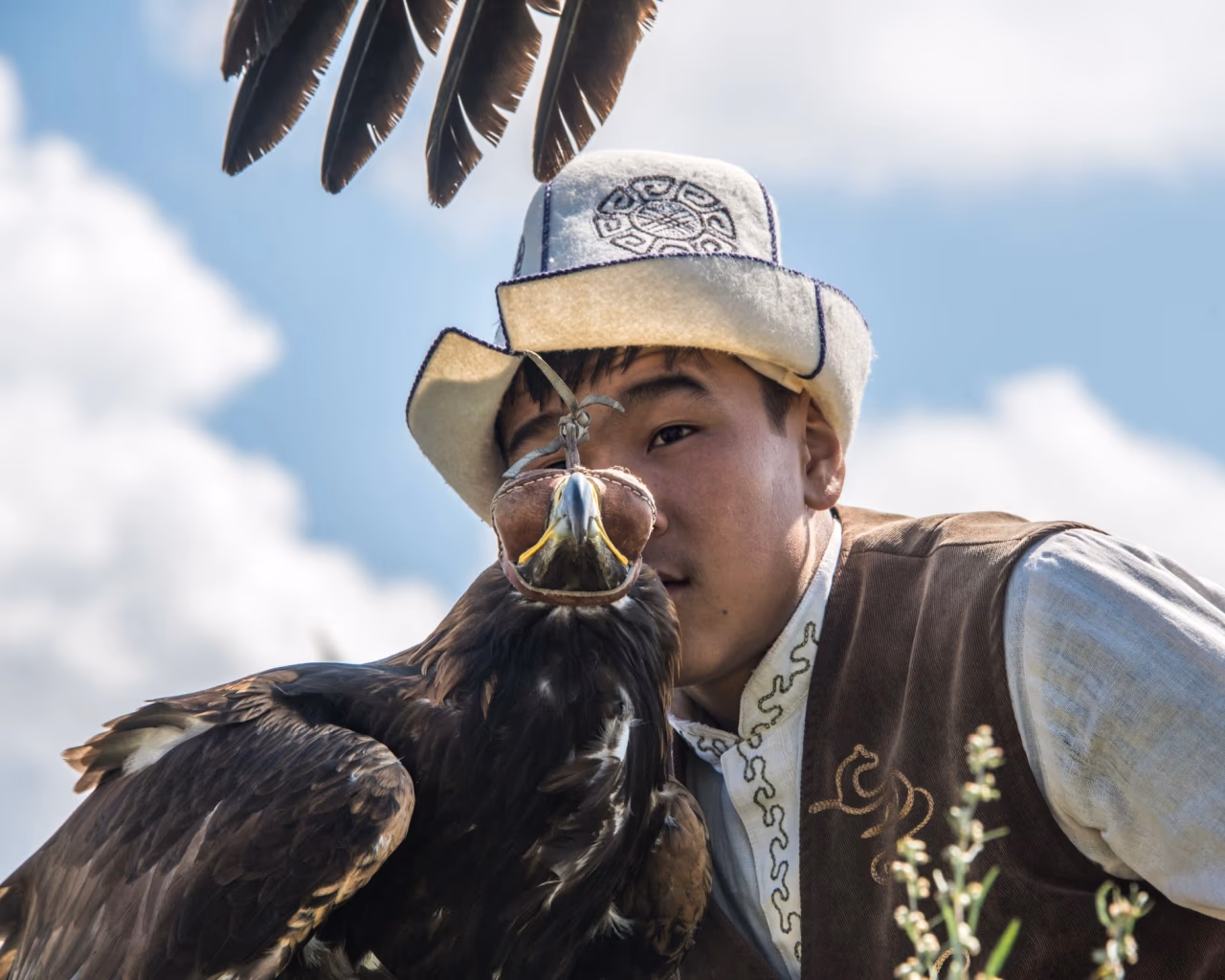 Kyrgyz eagle hunter in traditional attire with golden eagle perched on gloved arm.