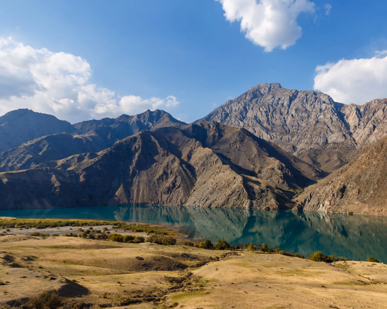 Naryn River flowing through rugged Kyrgyz mountains under a blue sky with scattered clouds.