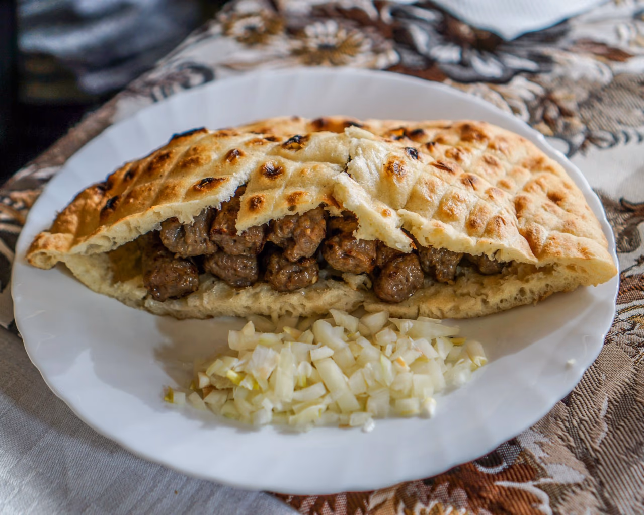 Bosnian ćevapi served in somun bread with onions – traditional Balkan dish on a white plate.