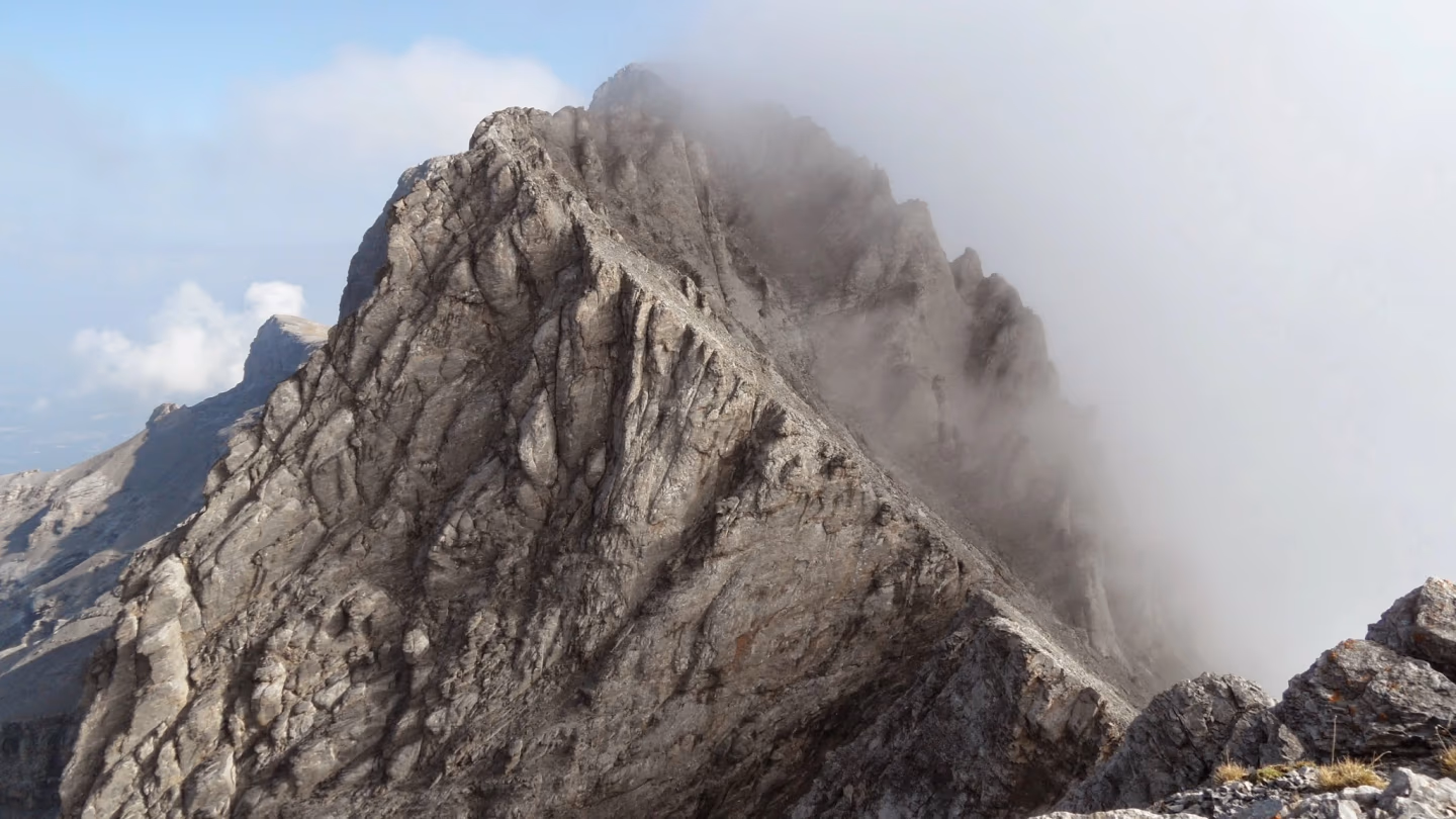 Dramatic mist-covered rocky ridge along a hiking trail on Mount Olympus, Greece, showcasing the rugged alpine terrain.