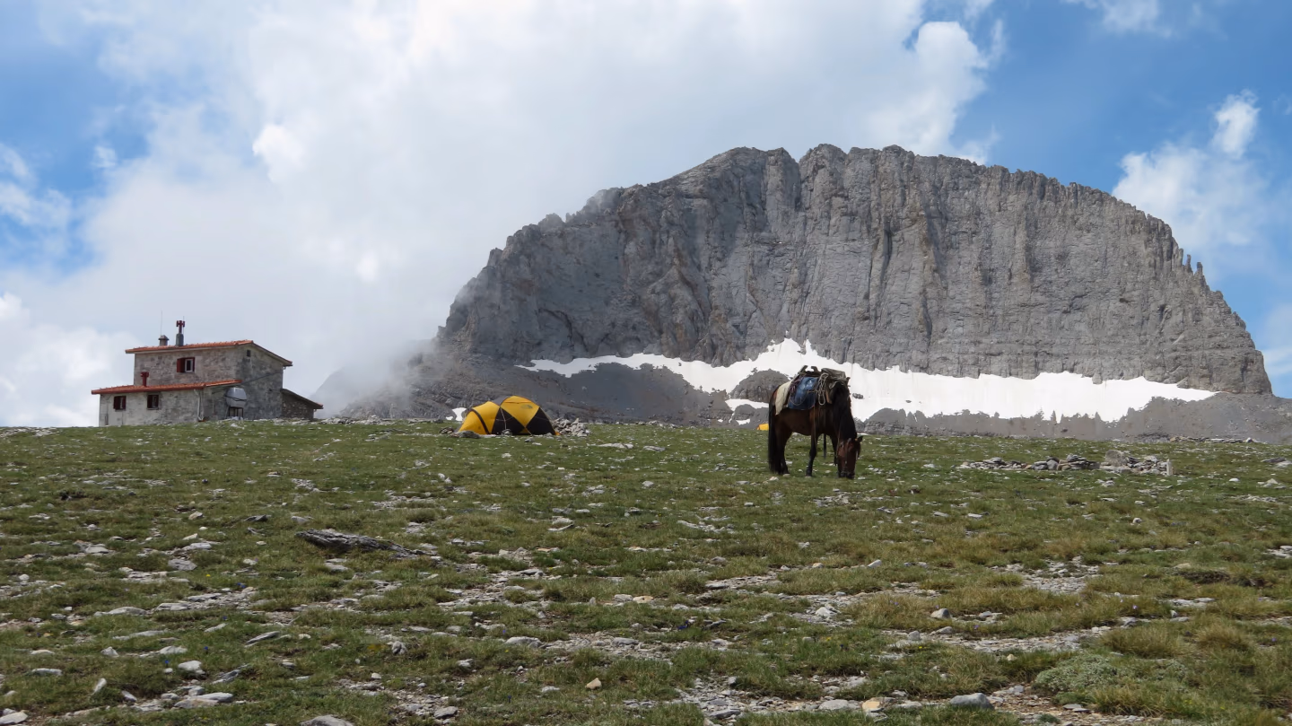 View of Stefani Peak, the Throne of Zeus, with Kakalos Mountain Hut and yellow tents on Mount Olympus, Greece.