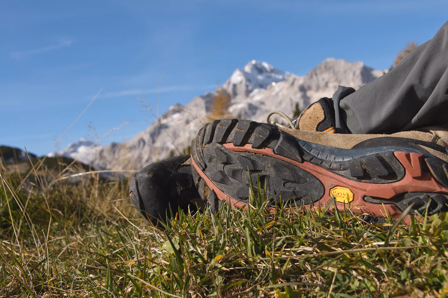 A pair of worn hiking boots resting on grass with a backdrop of the snow-capped peaks of the Julian Alps in Slovenia.