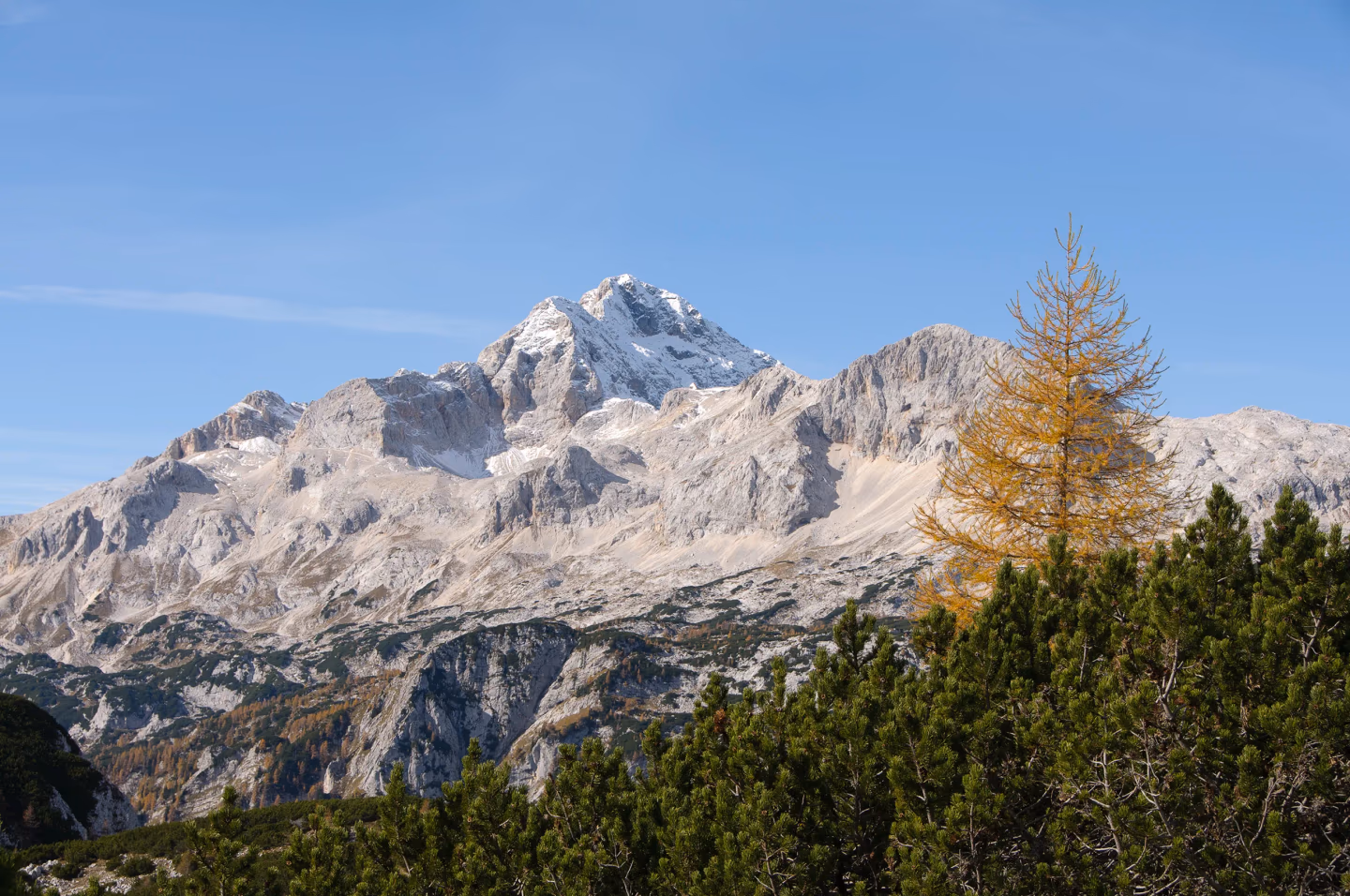 Hiker standing on a scenic mountain ridge in the Julian Alps, Slovenia, overlooking dramatic peaks and alpine valleys under a blue sky