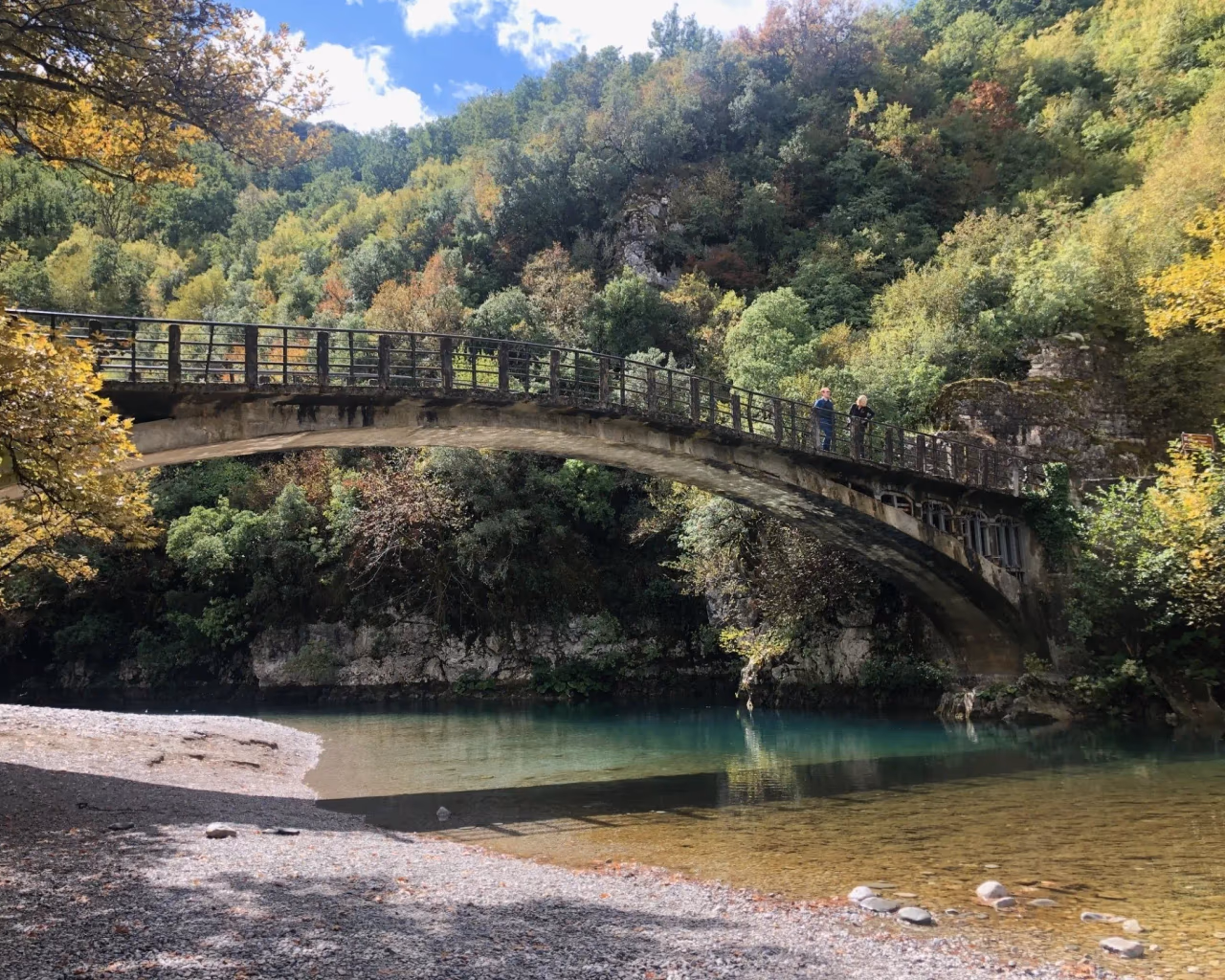 Stone bridge over Voidomatis River, reflecting autumn trees, in the heart of Zagori, Epirus, Greece.