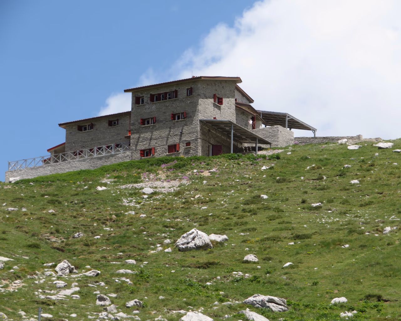 Stone mountain refuge with red shutters on a grassy hilltop in the Astraka region of Epirus, Greece.