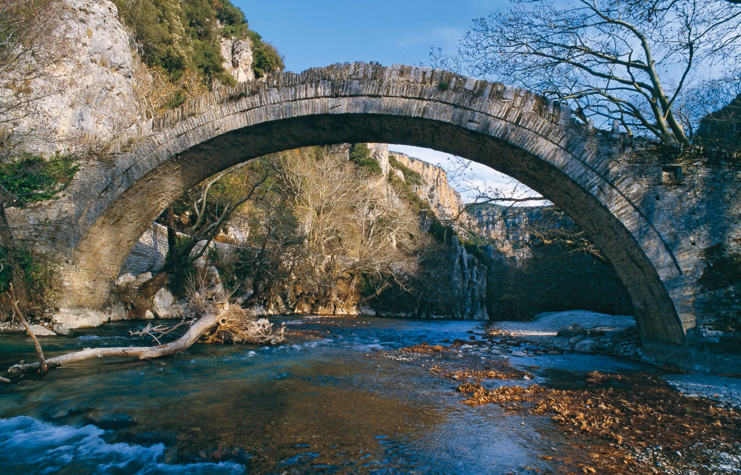 Stone arch bridge crossing the clear waters of Voidomatis River near Kleidonia, Epirus, Greece.