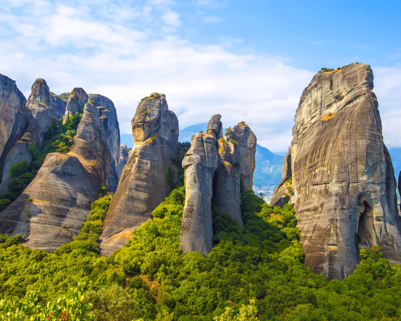 Towering rock formations in Meteora, Greece, with green forest nestled between the dramatic stone pillars.