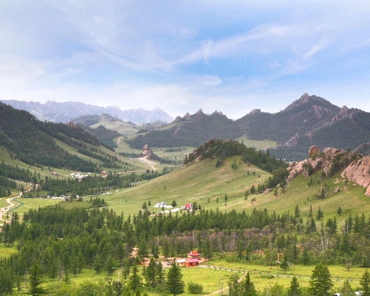 Rolling green hills, rocky cliffs, and scattered yurts in Terelj National Park, perfect for Mongolia trekking tours.