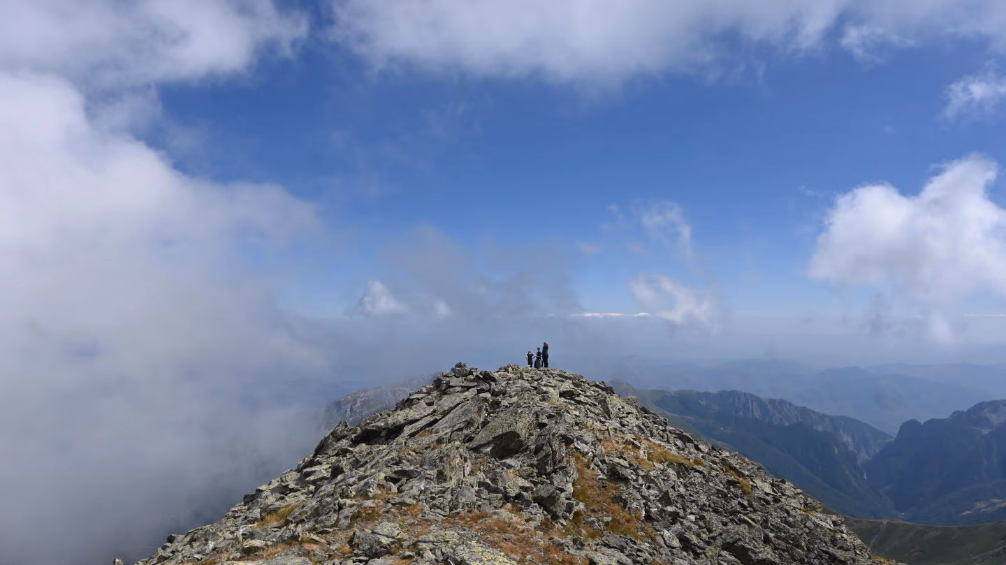 Hikers standing on a rocky peak with clouds around and vast mountain views along Kosovo’s Via Dinarica trail