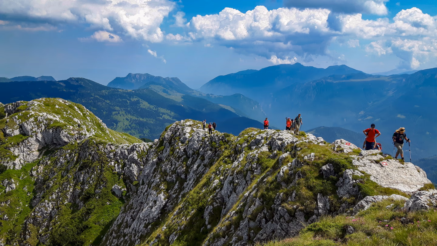 Trekkers walking a rocky ridge on the Via Dinarica trail in Kosovo, with panoramic mountain views.
