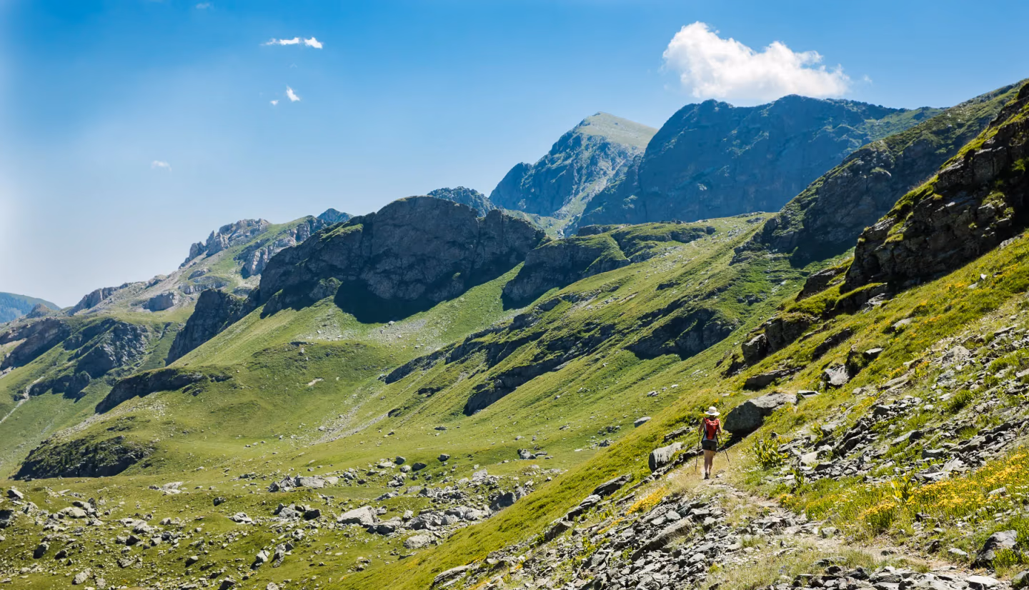 Solo hiker trekking a rocky slope along Kosovo’s Via Dinarica trail, surrounded by lush mountains.