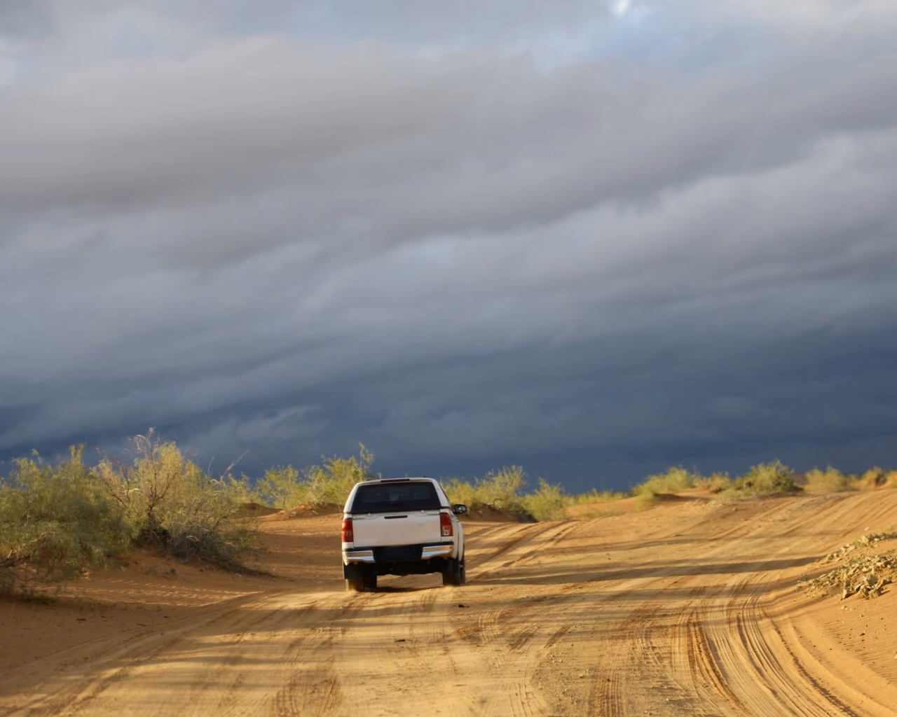 Off-road vehicle driving along sandy tracks in the Karakum Desert under storm clouds.